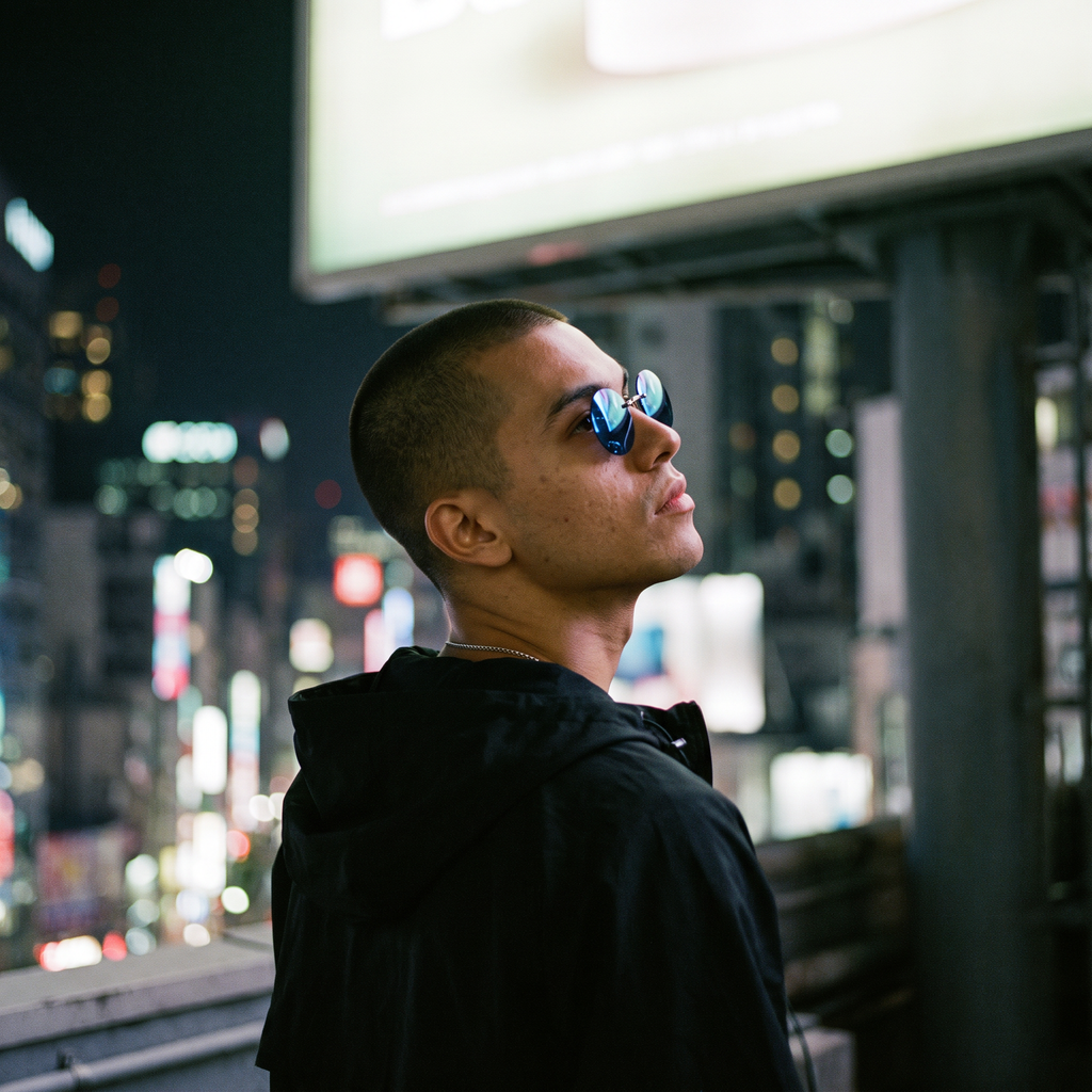 Round rimless clip-on sunglasses in blue mirror worn on a rooftop, looking up under a billboard