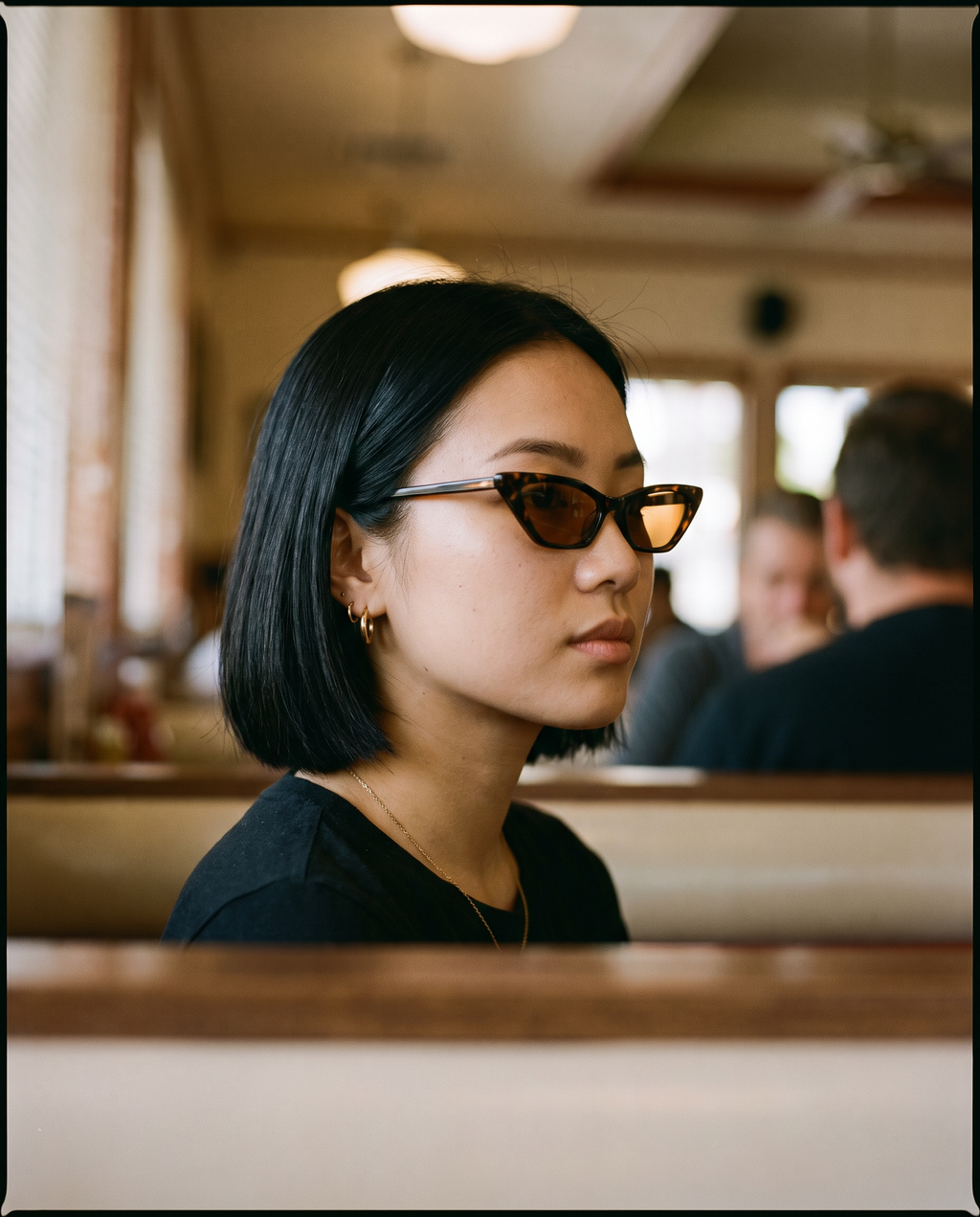 Small Cat Eye Retro 90s Sunglasses in Black Amber worn in a diner booth