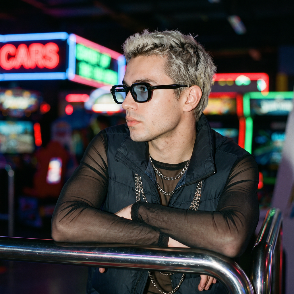 Man wearing blue-lens small square Y2K sunglasses at a neon arcade