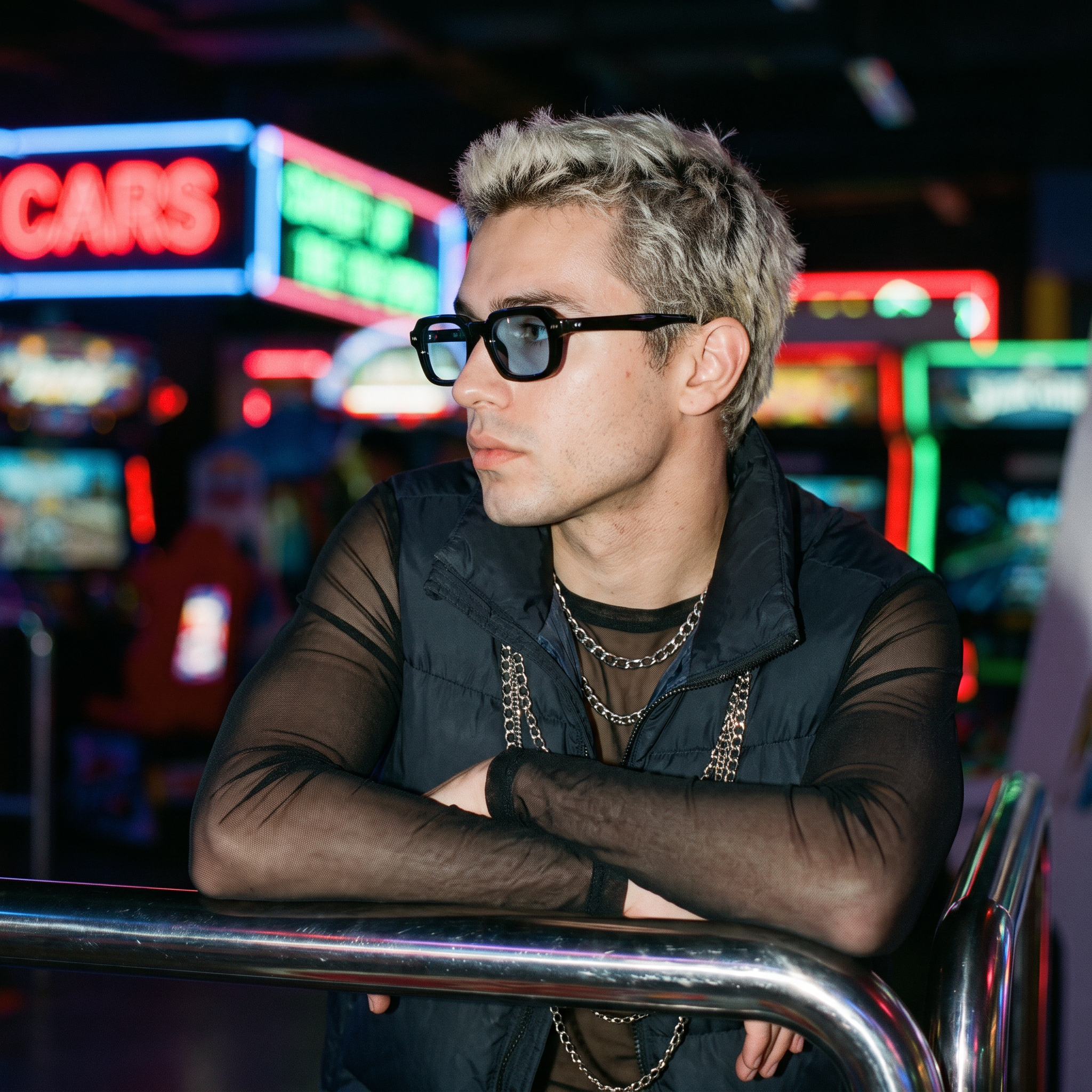 Man wearing blue-lens small square Y2K sunglasses at a neon arcade